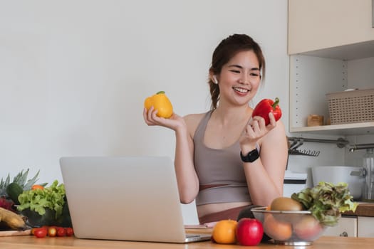 A woman is holding a laptop and two peppers in her hands. She is smiling and she is enjoying herself