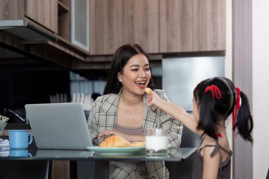 Working mom work from home office. Happy mother and daughter feed snacks to each other. businesswoman and cute child using laptop work freelancer workplace in home, Lifestyle family moment.