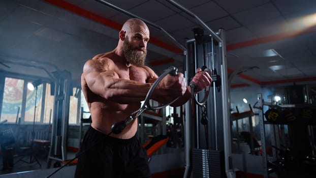 Bald Caucasian bodybuilder training chest using cable crossover in gym