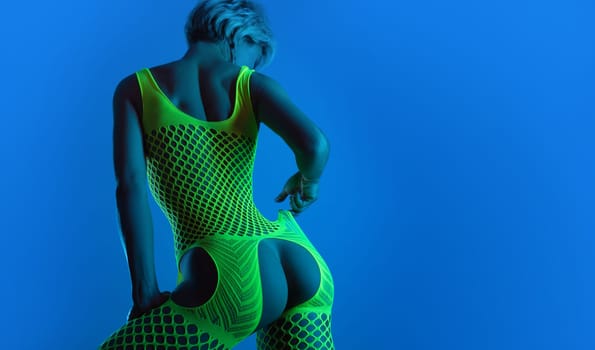 hot girl in erotic lingerie, a mesh bodysuit with an open crotch sexually poses with buttocks for a sex shop in neon blue light against a background of copy paste