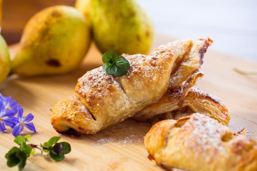 Sweet pastries, puff pastries with pears, on a wooden table .