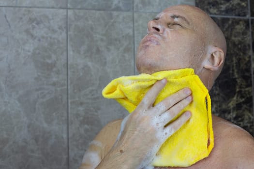 Bald man in shower washing his head with washcloth and foam, body cleanliness and skin care at home