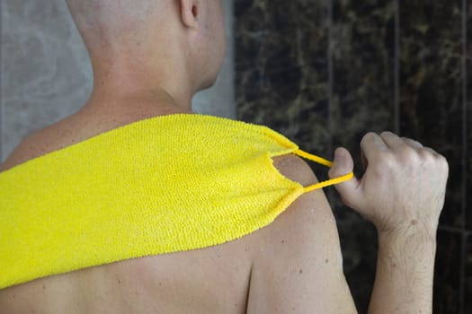 Man washes his back with special washcloth with handles, foam and cleanser to keep his skin clean in the shower