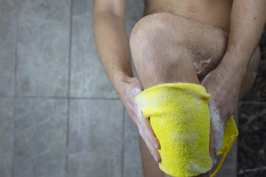 Male hands soaping hairy leg with a washcloth with foam, body care and skin care in the shower, cleanliness and personal hygiene of man