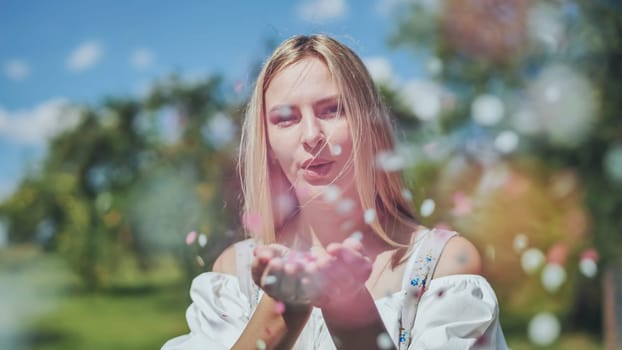 A girl blows a multi-coloured paper confetti out of her hands