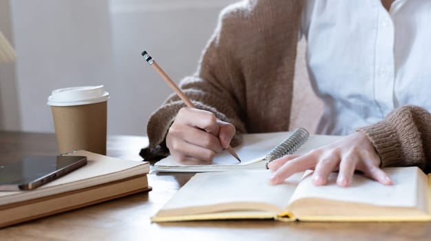 Asian students study online, take notes, do homework, study online from home on a wooden table in the house..