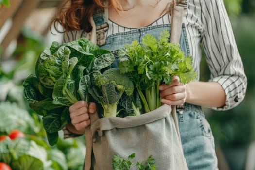 A woman is holding a bag of vegetables, including broccoli and cilantro. She is wearing blue overalls and has red hair