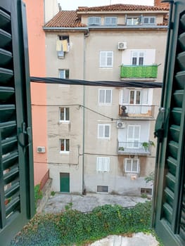 Old house with old balconies through the green window. High quality photo. Looking through the window in the morning. View inside of the buildings