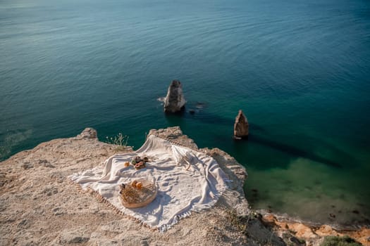 A white blanket is spread out on a beach near the water. The blanket is on a rock and there are some oranges and apples on it. The scene is peaceful and relaxing, with the ocean in the background