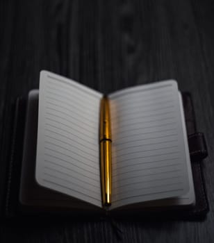 Subject shooting - Notepad and gold pen. Blank notepad on a darck wood. High quality photo