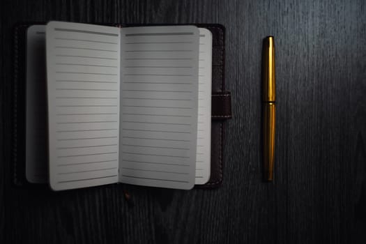 Subject shooting - Notepad and gold pen. Blank notepad on a darck wood. High quality photo