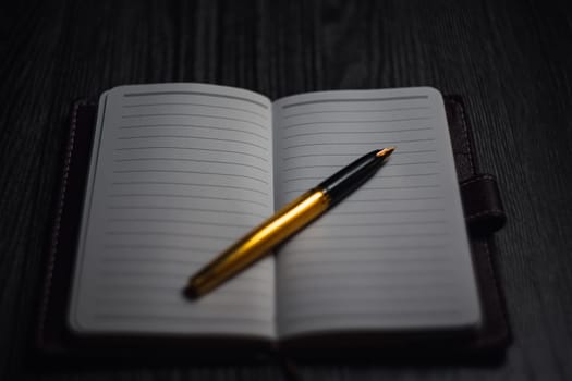 Subject shooting - Notepad and gold pen. Blank notepad on a darck wood. High quality photo