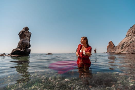 A woman in a red dress is sitting in the water. The water is clear and the sky is blue