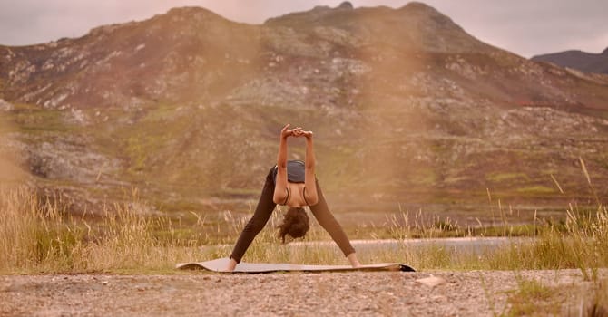 Yoga, woman and stretching outdoor for fitness, wellness and mindfulness on mountain. Sunset, zen chakra and calm female yogi practicing pilates, balance and training, for health and wellbeing.