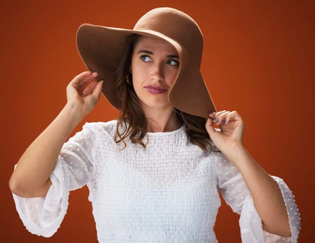 Woman, hat and studio with thinking for fashion with fancy, trendy and summer outfit for vacation style inspiration. Stylish, brown background and trends with clothes for gorgeous with self esteem.