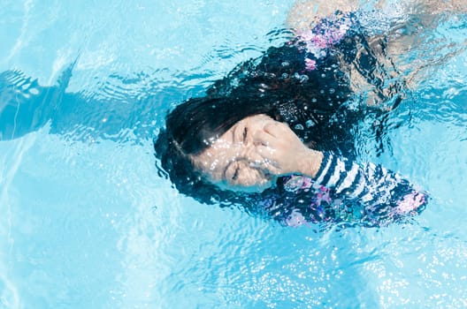 The girl in the pool swimming underwater smiling and holding her nose