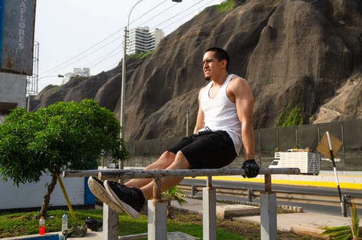 Handsome man exercising on parallel bars on the street outdoors