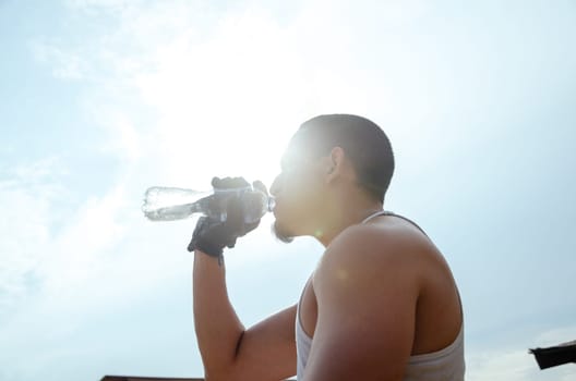 Young exhausted athlete drinking fresh water to cool off during a running track