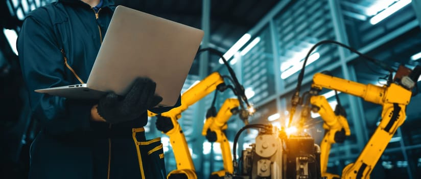 MLB Engineer use advanced robotic software to control industry robot arm in factory. Automation manufacturing process controlled by specialist using IOT software connected to internet network.