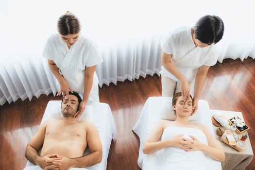 Caucasian couple enjoying relaxing anti-stress head massage and pampering facial beauty skin recreation leisure in dayspa modern light ambient at luxury resort or hotel spa salon. Quiescent