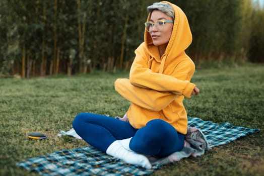 A cute girl with glasses in an orange hoodie is sitting in a park in nature expressing kind emotions