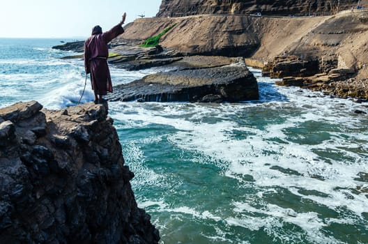 Man dressed as a friar throws himself off a cliff and head into the ocean at sunset