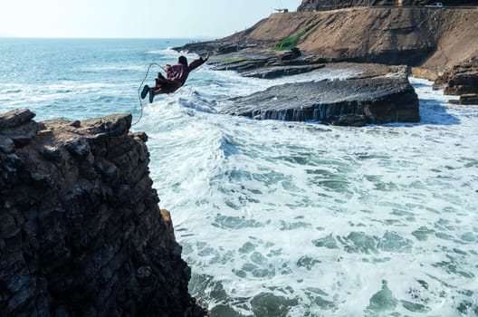 Man dressed as a friar throws himself off a cliff and head into the ocean at sunset