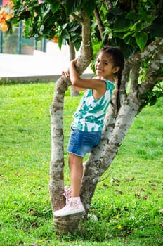 Cute little girl is playing in the park climbing on a tree