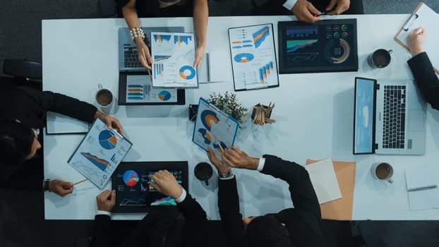 Top down aerial view of business people discussing about financial strategy on table with document and tablet display investment statistic at meeting. Diverse team brainstorm about plan. Directorate.