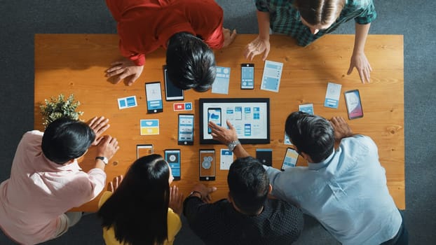 Top view of software developer team looking Ux Ui design for mobile phone interface from tablet while comparing and planning wireframe prototype designing together at creative workplace. Convocation.