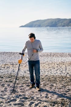 Young man with a metal detector walks along the beach, sweeping it over the pebbles. High quality photo