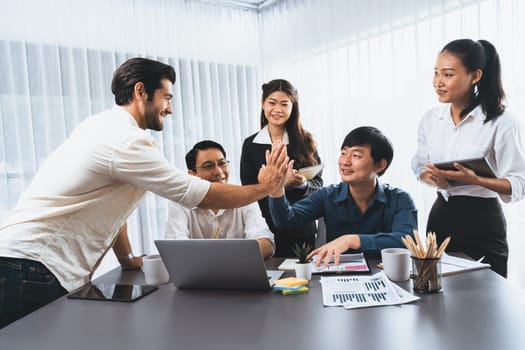 Diverse group of office employee worker high five after making agreement on strategic business marketing planning. Teamwork and positive attitude create productive and supportive workplace. Prudent