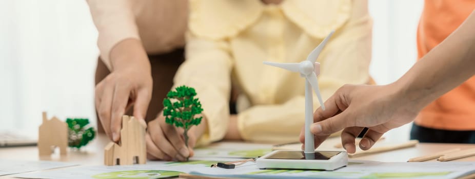 Windmill model represented using renewable energy placed during presenting green business on table with wooden block and environmental document scatter around. Closeup. Delineation.