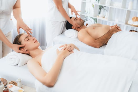 Caucasian couple enjoying relaxing anti-stress head massage and pampering facial beauty skin recreation leisure in dayspa modern light ambient at luxury resort or hotel spa salon. Quiescent