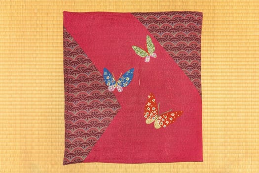 Texture photography of a Japanese square-shaped zabuton cushion decorated with embroidered patterns of butterflies and flowers used for sitting in seiza or agura position on a rice straw tatami.