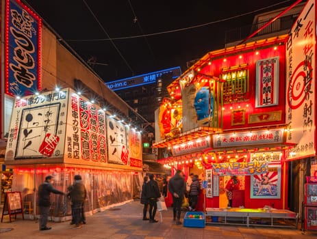 osaka, japan - dec 04 2023: Shooting game attraction store and Japanese kushikatsu deep-fried skewered specialities restaurant illuminated at night in the Tsutenkaku Street of Shinsekai district.