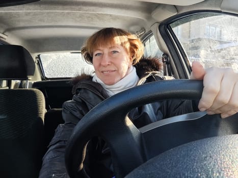 A woman in a car taking a selfie while enjoying a drive. Female driver in warm jacket posing inside car in warm jacket on a cold day