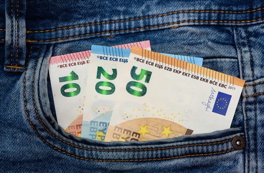 10, 20 and 50 euro bills coming out of the back pocket of a pair of jeans