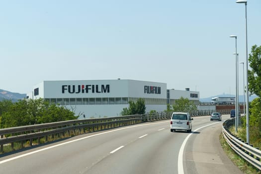 Barcelona, Spain - May 24, 2023: A car drives on a highway past the Fujifilm factory, showcasing the buildings exterior under clear, blue skies.