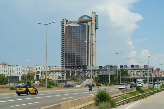 Barcelona, Spain - May 24, 2023: Cars and a taxi travel on a multi-lane road beneath clear skies, with the Hesperia Tower visible in the background.