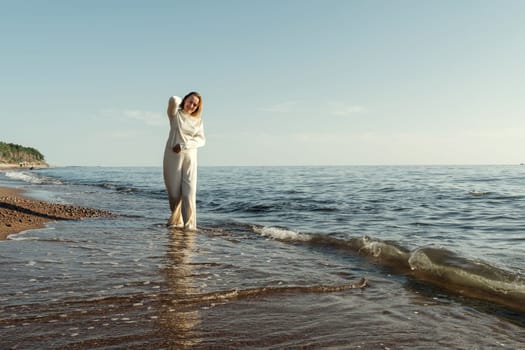 A woman standing waist-deep in the water at a sandy beach, with waves gently splashing around her.