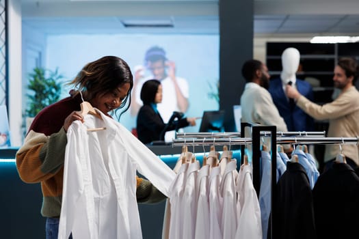 African american woman trying on shirt, checking size and fit while shopping in clothing store. Customer examining apparel while choosing formal outfit in mall fashion boutique