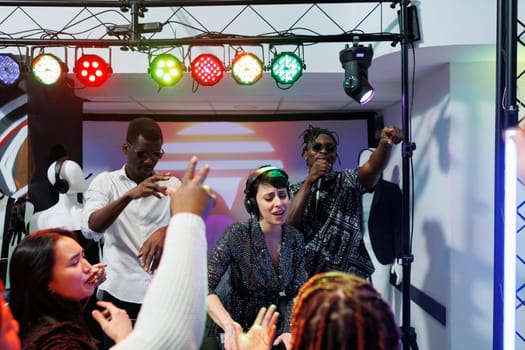 Group of diverse musicians playing on stage and engaging clubbers crowd to party in nightclub. Music band performing while young people dancing and cheering on dancefloor in club