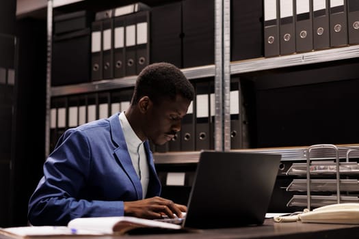 African american businessman analyzing administrative files, reading accountancy report in corporate depository. Bookkeeper working late at night at bureaucracy record in storage room