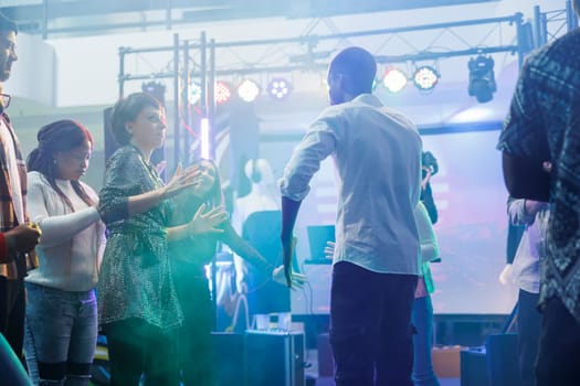 Man and woman friends showing fun moves at dance battle while partying in nightclub. Dancers improvising on dancefloor illuminated with colorful lights while celebrating in club