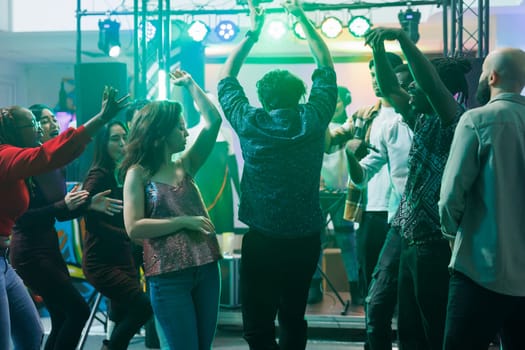 Active people dancing and raising hands while partying in nightclub. Young men and women moving to electronic music beats and relaxing on crowded dancefloor at discotheque