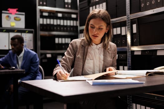 Police officer analyzing fraude case evidence, checking files with confidential information. Private investigator in formal suit searching for clues to catch suspect, working overtime in arhive room