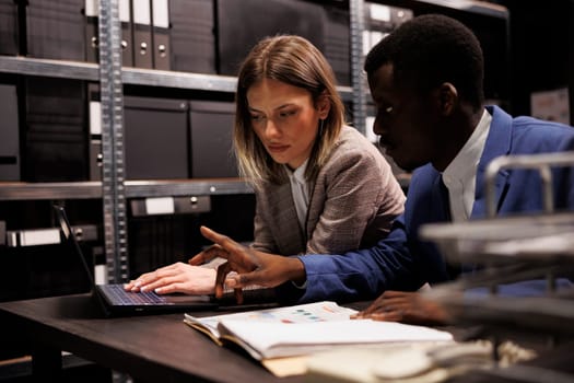 Investigators working late at night in arhive room, analyzing criminal case evidence searching for new clues. Detectives examining investigation files, reading victim report. Law enforcement concept