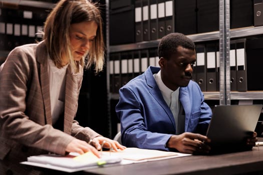 Diverse inspectors working at fraude case, checking company surveillance footage searching for new clues in arhive room. Private detectives reading confidential files, analyzing evidence