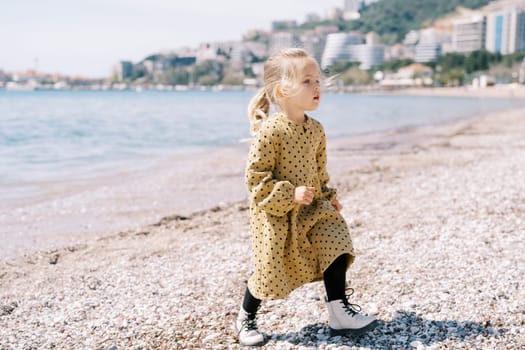 Little girl walks along a pebble beach and looks away. High quality photo